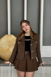 a lady in a black top, a tweed brown jacket and a brown pleated skirt